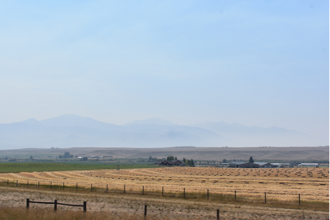 A freshly cut and baled hay field surrounded by vast farmland with low mountains in the distance